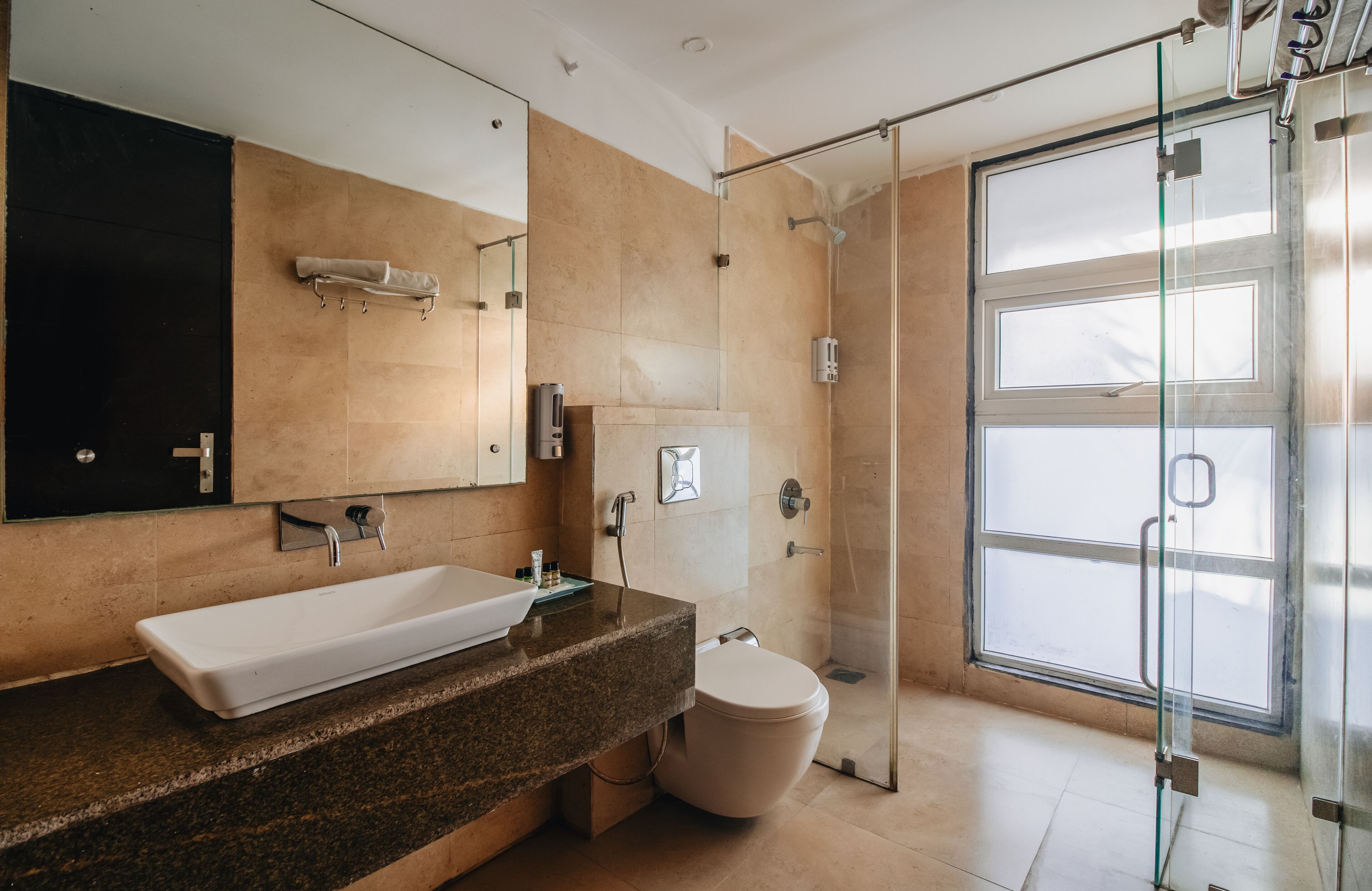 A modern bathroom with a large mirror, a white sink, a toilet, and a glass-enclosed shower.