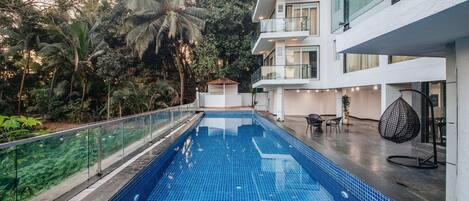 A modern building with a swimming pool, surrounded by lush greenery and palm trees.