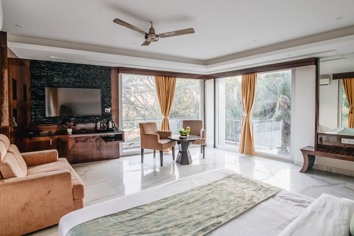 Quarto de hotel moderno com uma cama grande, área de estar com mesa, televisão de tela plana e varanda com cortinas.