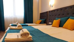A hotel room with two beds, each with teal and yellow bedding, and a large window with curtains. - Sharkov Family Hotel  (Garmen)