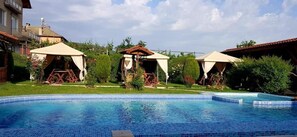 A swimming pool with a tiled edge, surrounded by greenery and a building with a red roof. - Sharkov Family Hotel  (Garmen)