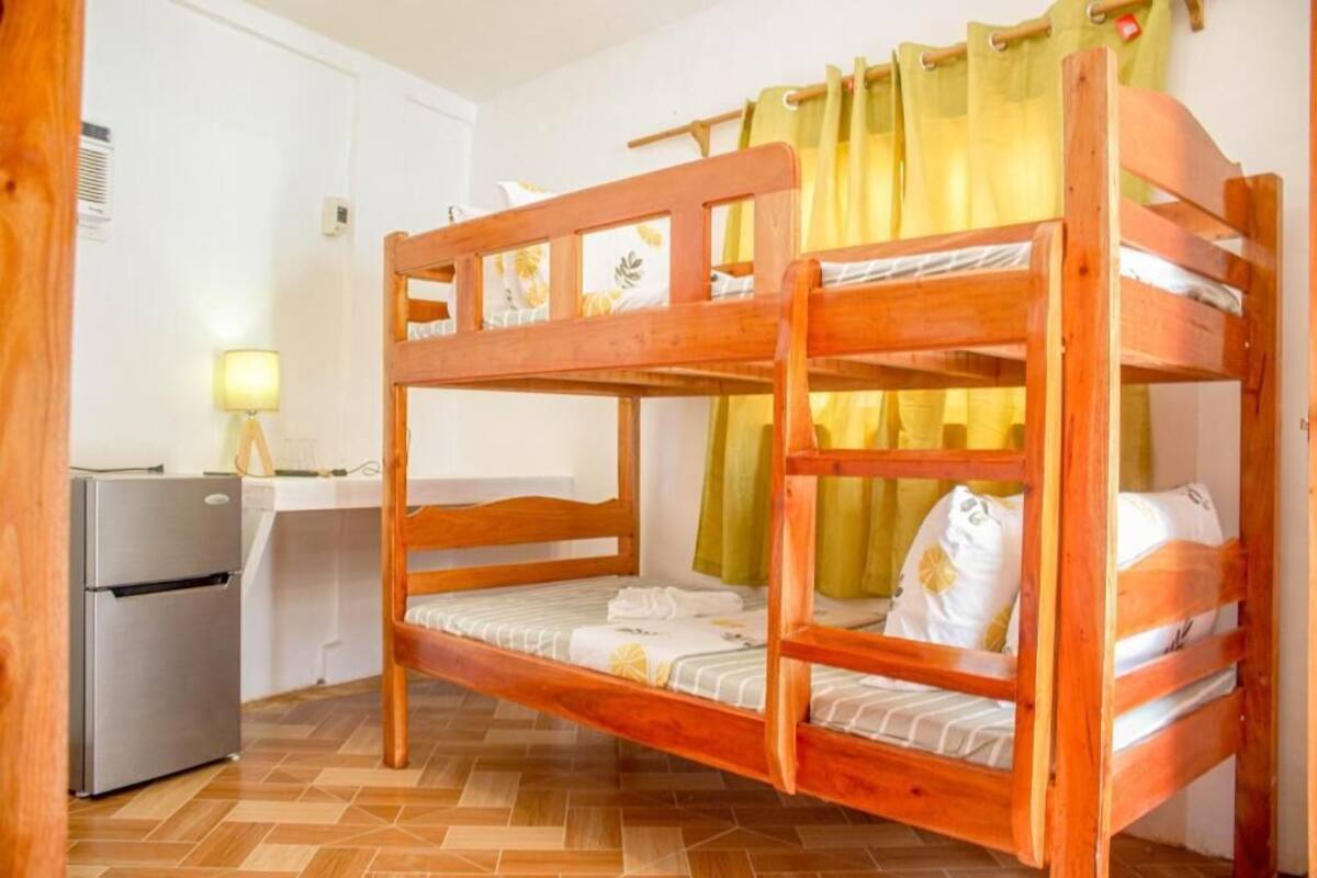 A bunk bed with a desk and a refrigerator in a room with wooden flooring.
