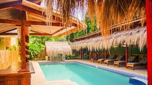 Un espace piscine doté d’un toit de chaume, de chaises longues et d’une terrasse en bois.
