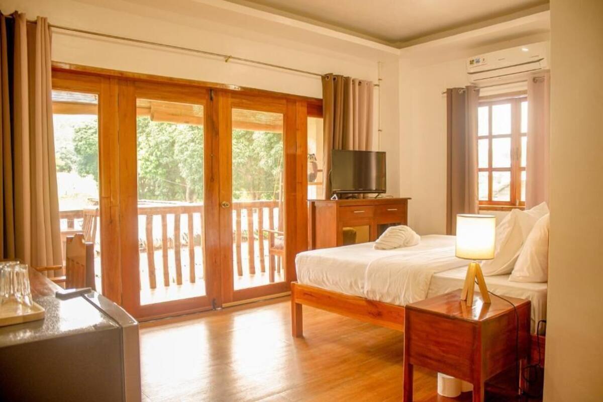 A bedroom with a bed, bedside table, TV, and a balcony with wooden railings.
