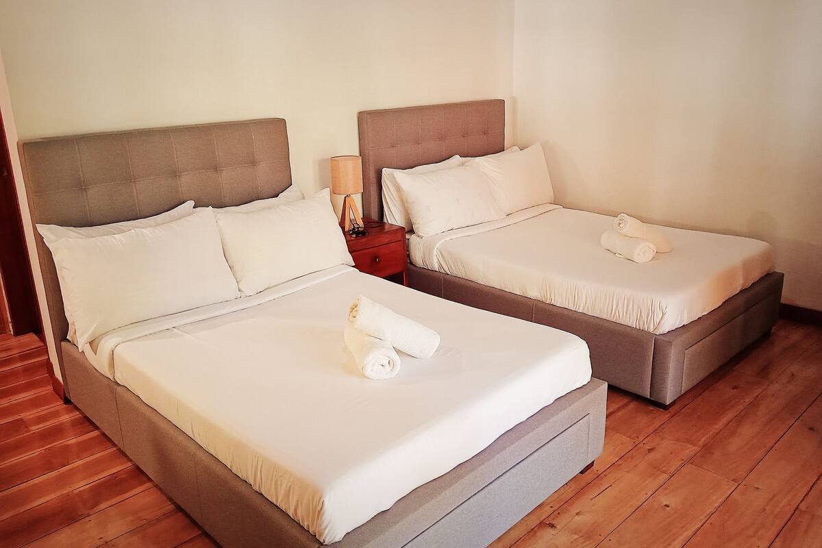 Two single beds with headboards, a nightstand with a lamp, and a wooden floor.