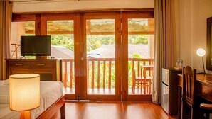 Une chambre d’hôtel comprenant un lit, un bureau avec un ordinateur, une télévision et un balcon doté d’une rambarde en bois.