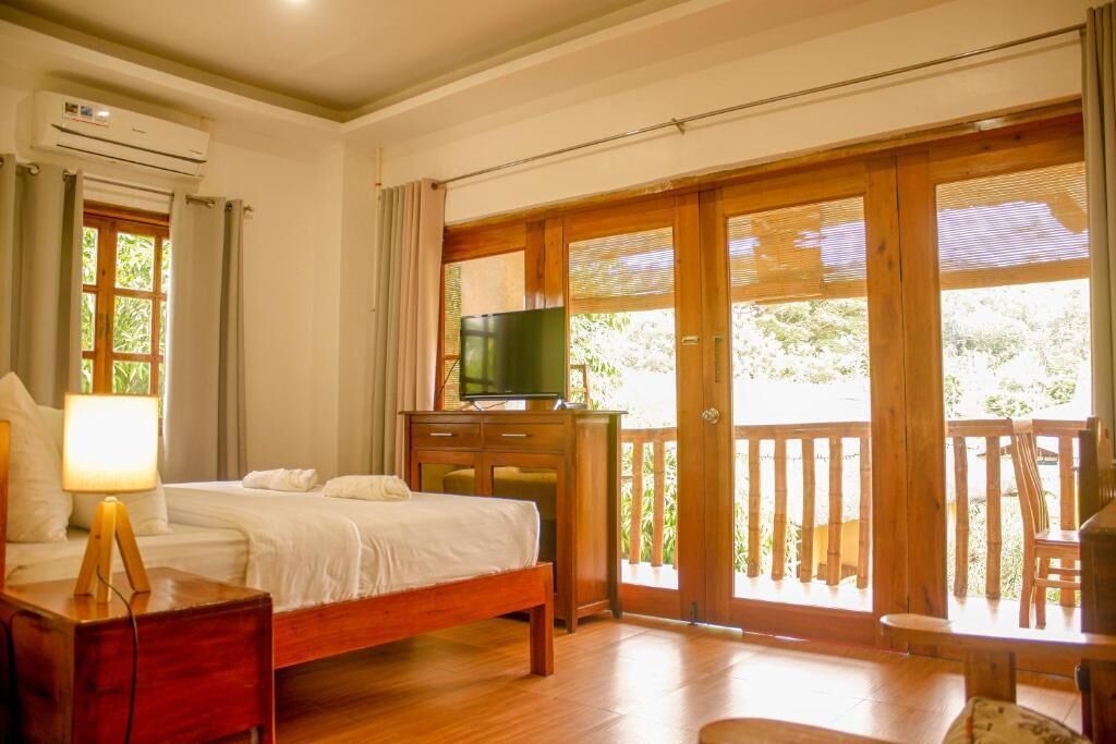 A bedroom with a bed, a TV on a wooden cabinet, and a balcony with a wooden railing.