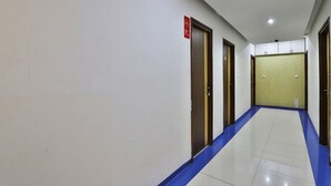 Un couloir aux murs blancs, au sol carrelé de bleu, et dont les portes donnent accès aux différentes pièces.