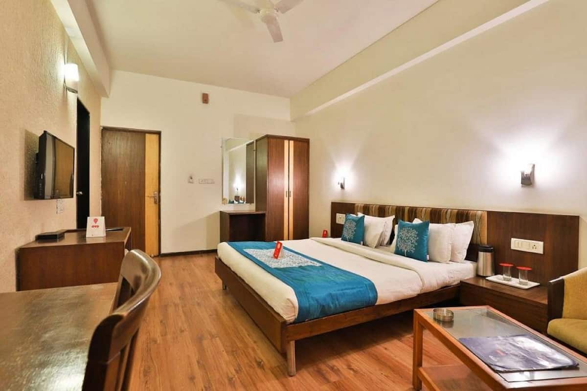 A hotel room with a bed, bedside table, chair, desk, and a television.