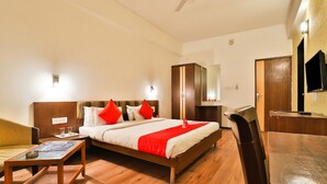 Une chambre d’hôtel avec un lit en bois, un bureau en bois, une chaise, une petite table et un téléviseur.
