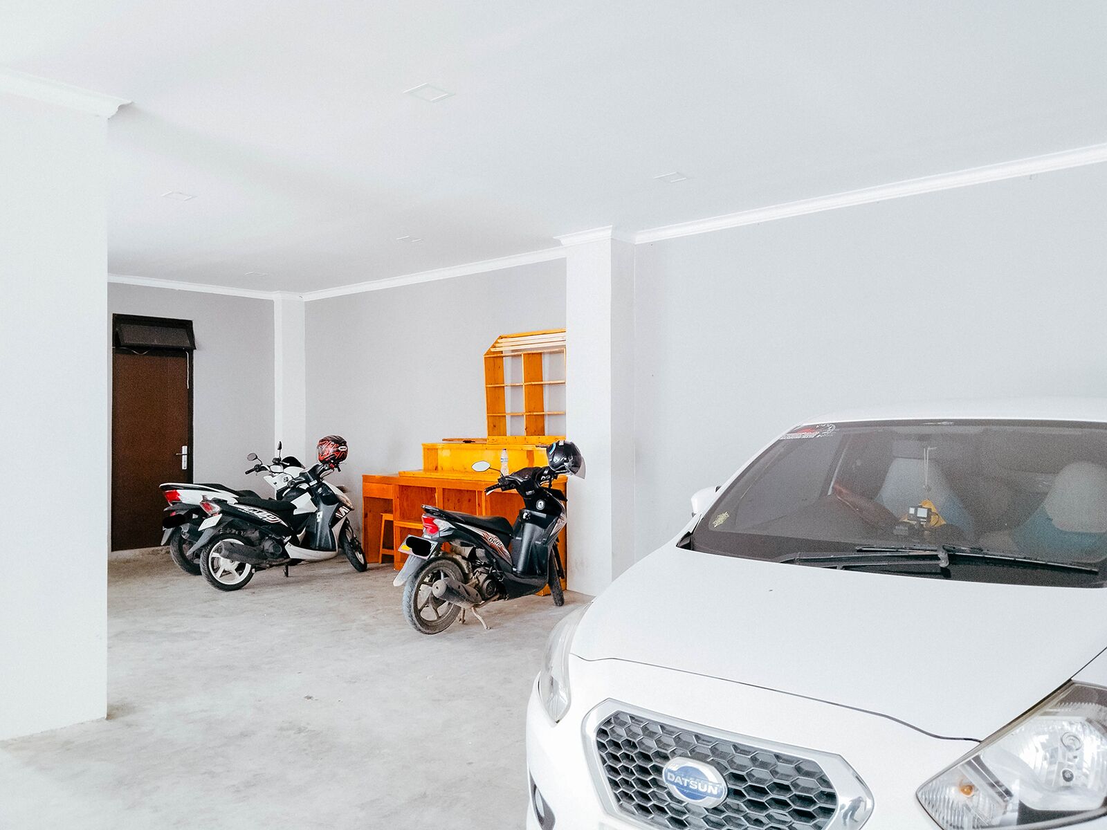 A white car parked in a garage with two motorcycles and a wooden workbench.
