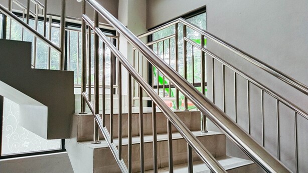 Een moderne trap met metalen leuningen en beige treden, die uitkomt op een plateau met een glazen deur.