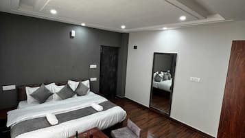 Una habitación de hotel moderna con una cama grande, una mesita con una botella y vasos, y un espejo en la pared.