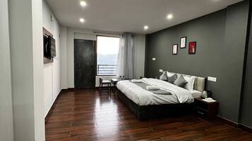 A modern bedroom with a large bed, a desk, and a view of the outdoors.