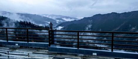 A view from a balcony with a metal railing, overlooking mist-covered mountains and a forested area.
