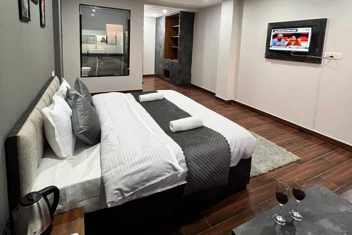 Una habitación de hotel moderna con una cama grande, televisión, mesita de café y vista a la cocina.