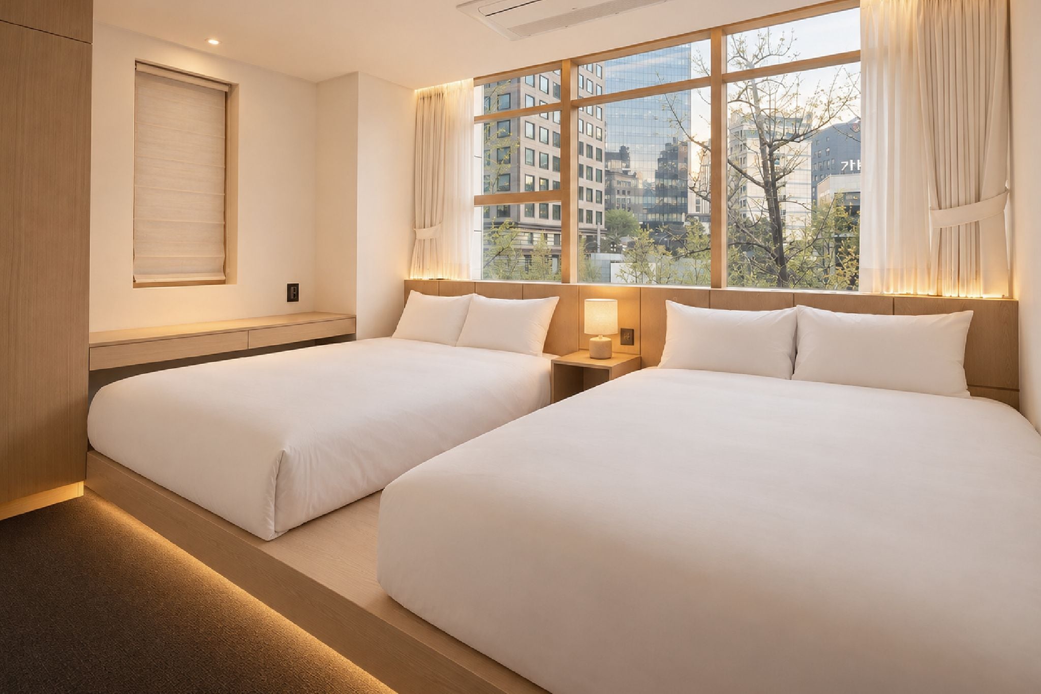 Quarto de hotel com duas camas, janela com cortinas e vista para a cidade.