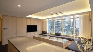 Une chambre d’hôtel moderne dotée d’une grande fenêtre, d’un téléviseur à écran plat, d’un coin salon avec des coussins et d’une table basse en verre.