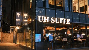 Un hôtel moderne doté d’une façade en verre, d’une enseigne lumineuse et d’un intérieur visible, avec des espaces aménagés pour s’asseoir.