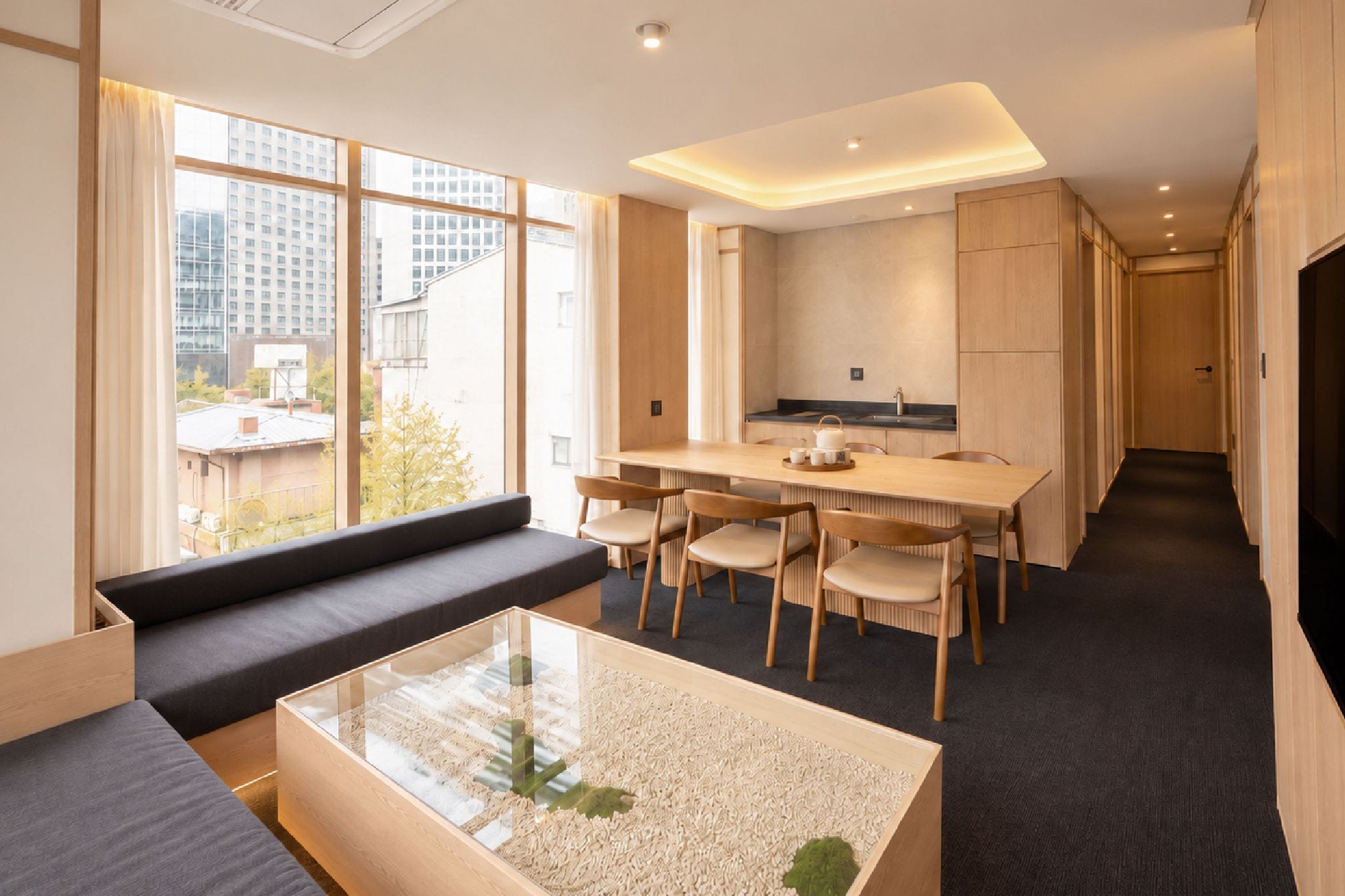 A modern interior with a sofa, a glass coffee table, a dining area with chairs, and a kitchen.