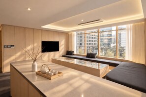 A modern hotel room with a large window, a flat-screen TV, a seating area, and a kitchen counter with tea set. - UH Suite Seoul Deoksugung (Seoul)