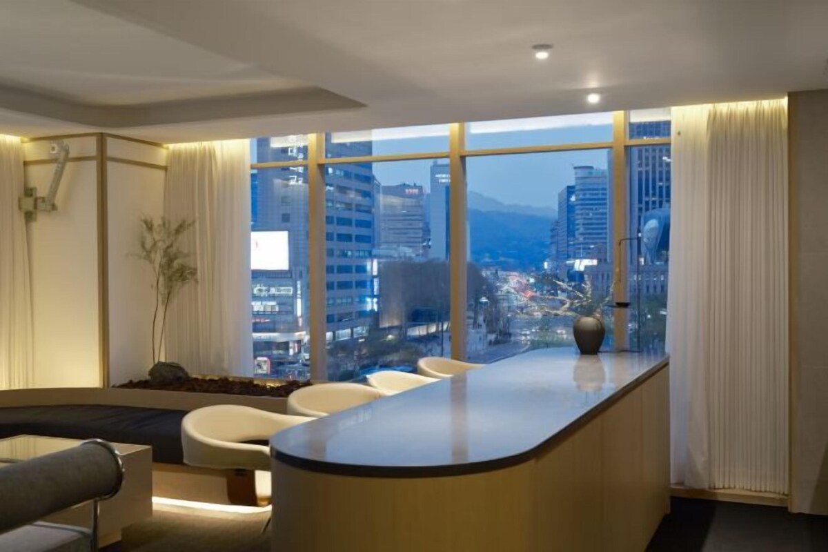 Eine moderne Hotelhalle mit einer gebogenen Rezeption, einer Sitzecke und großen Fenstern mit Blick auf die Stadt.