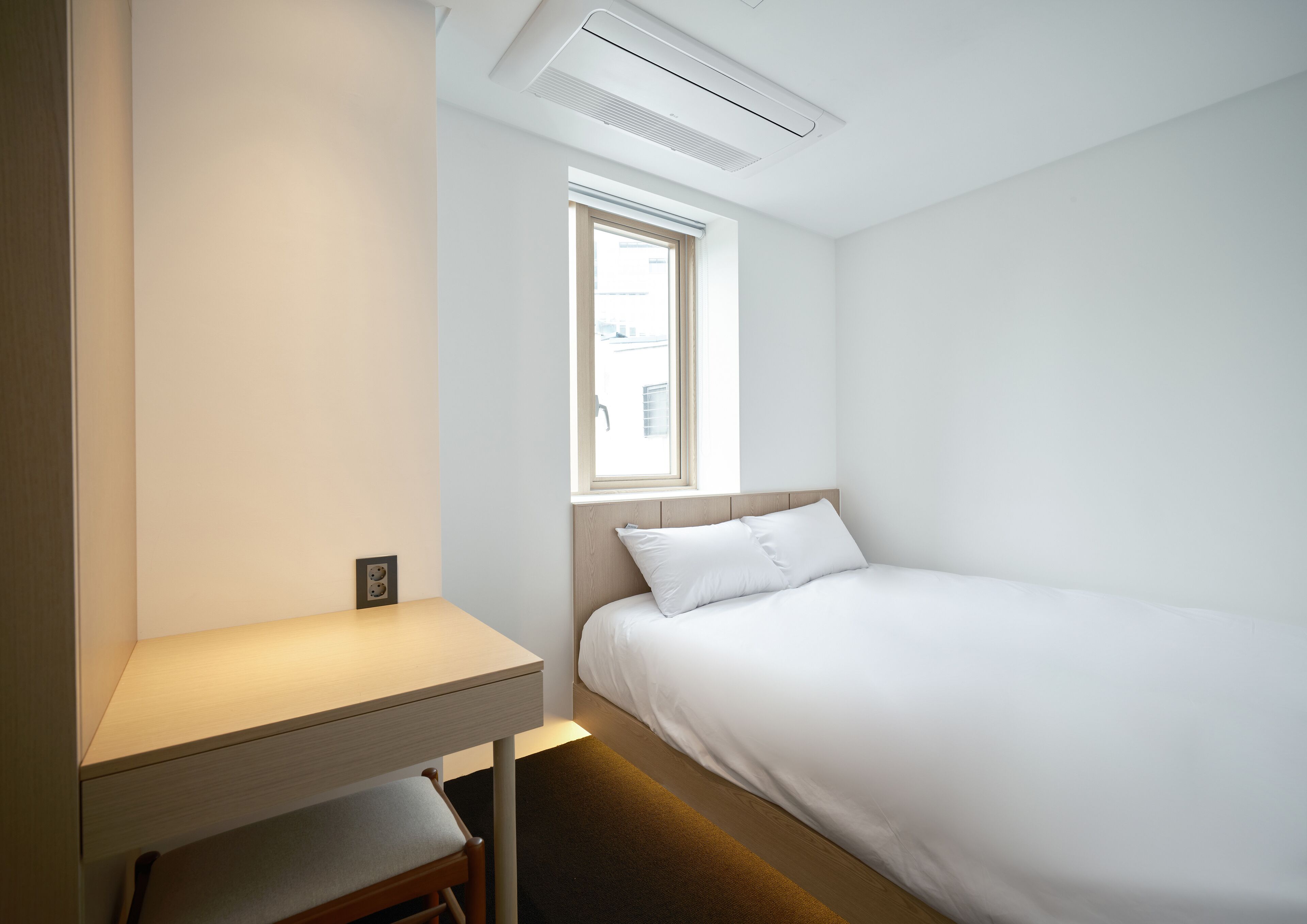 A minimalist room with a bed, a desk, and a window.