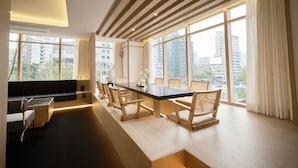 Un espace de restauration moderne, doté d’une longue table, de plusieurs chaises et de grandes fenêtres offrant une vue sur la ville.