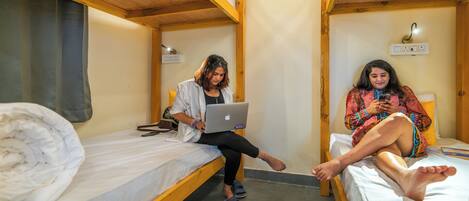 Une chambre de dortoir avec deux lits superposés, un ordinateur portable sur l’un des lits et une personne utilisant un téléphone intelligent sur l’autre.