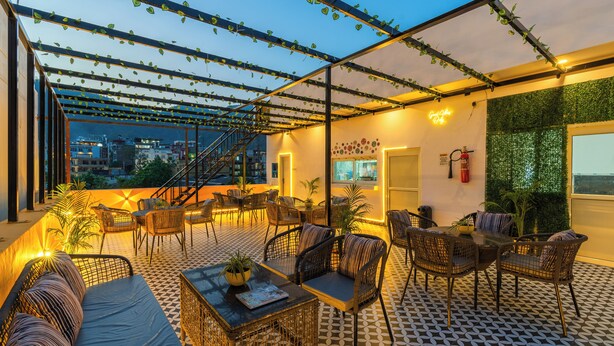 An outdoor seating area with wicker furniture, a patterned floor, and a view of the cityscape. - The Social Stays Rishikesh (Narendranagar)