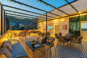 Un espacio al aire libre con mobiliario de mimbre, piso estampado y vista panorámica de la ciudad.