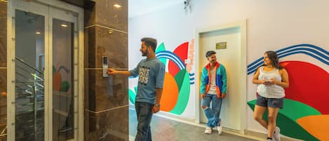 An indoor corridor with a glass elevator, a colorful wall mural, and a tiled floor.