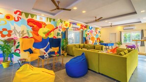 A vibrant living room with colorful murals, a yellow armchair, green sofas, and a blue bean bag. - The Social Stays Rishikesh (Narendranagar)