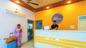 A reception desk with a sign that reads "Get Bizzing9" and a woman standing next to a blue suitcase. - The Social Stays Rishikesh (Narendranagar)