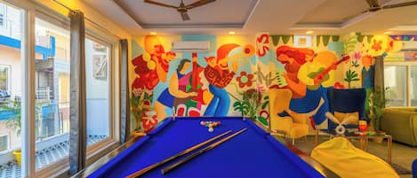 A pool table with pool cues and balls, a ceiling fan, and a colorful mural on the wall.
