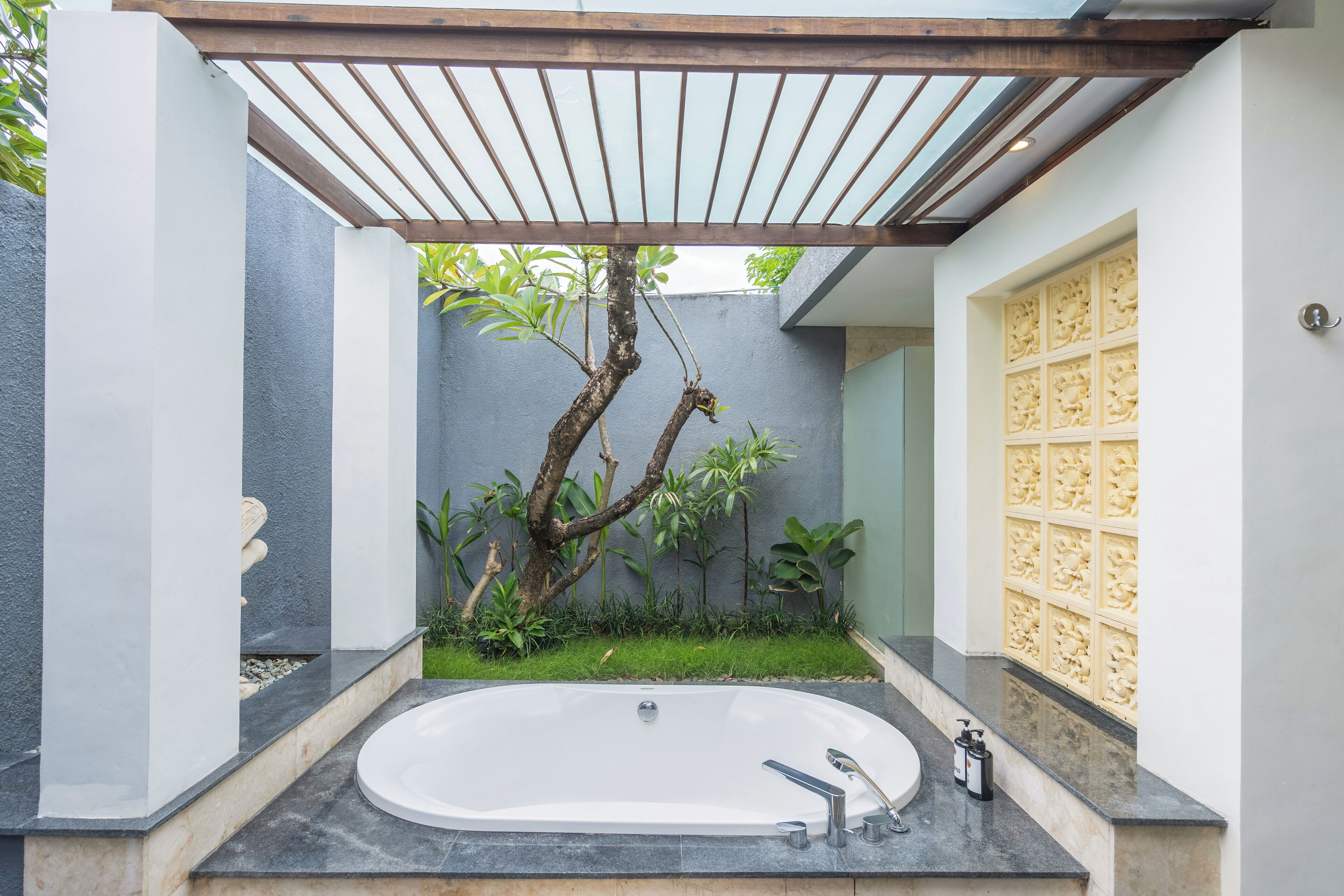 A modern bathroom with a freestanding bathtub, a wooden pergola, and a decorative wall panel.