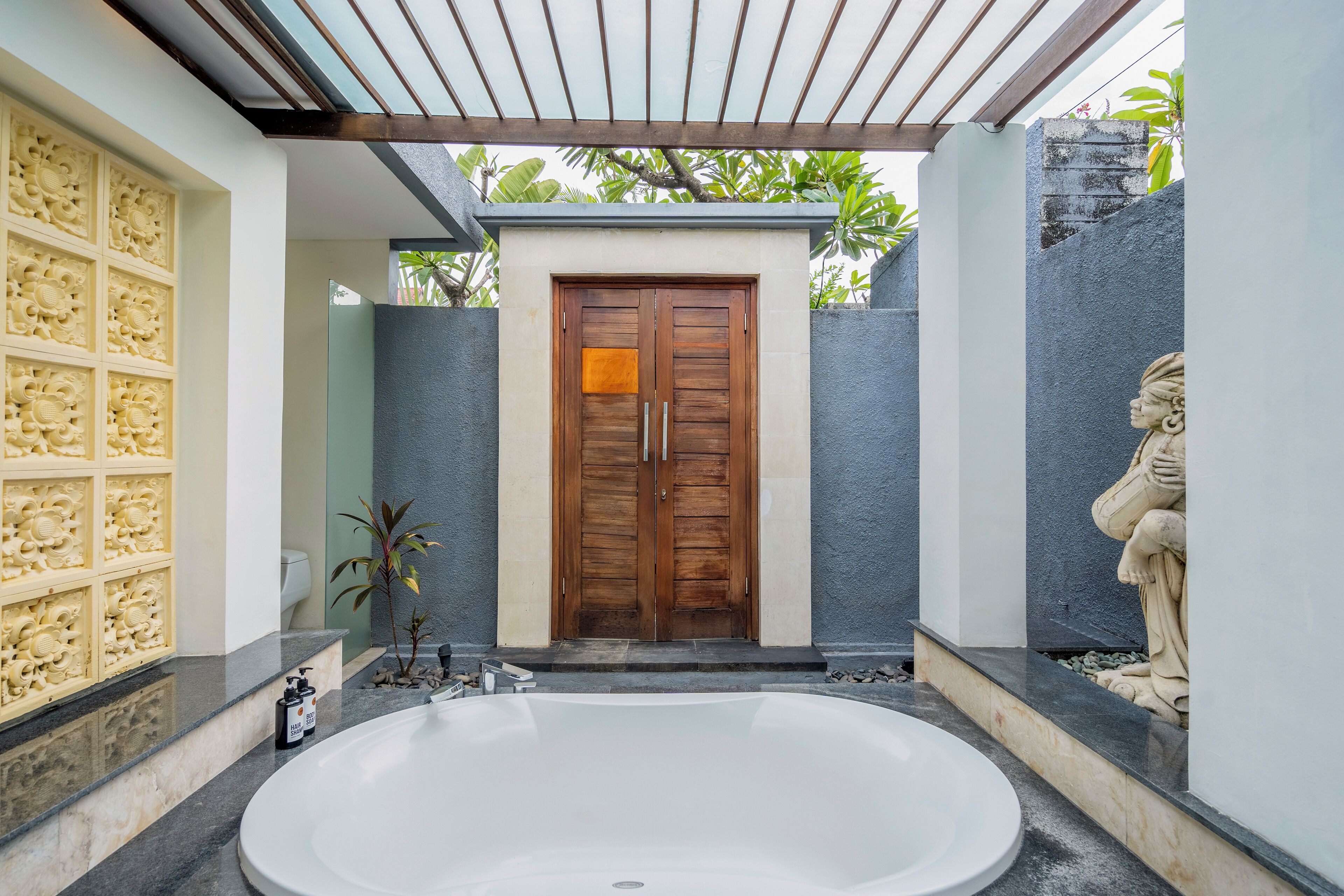 A modern bathroom with a large bathtub, a wooden door, and a stone statue.