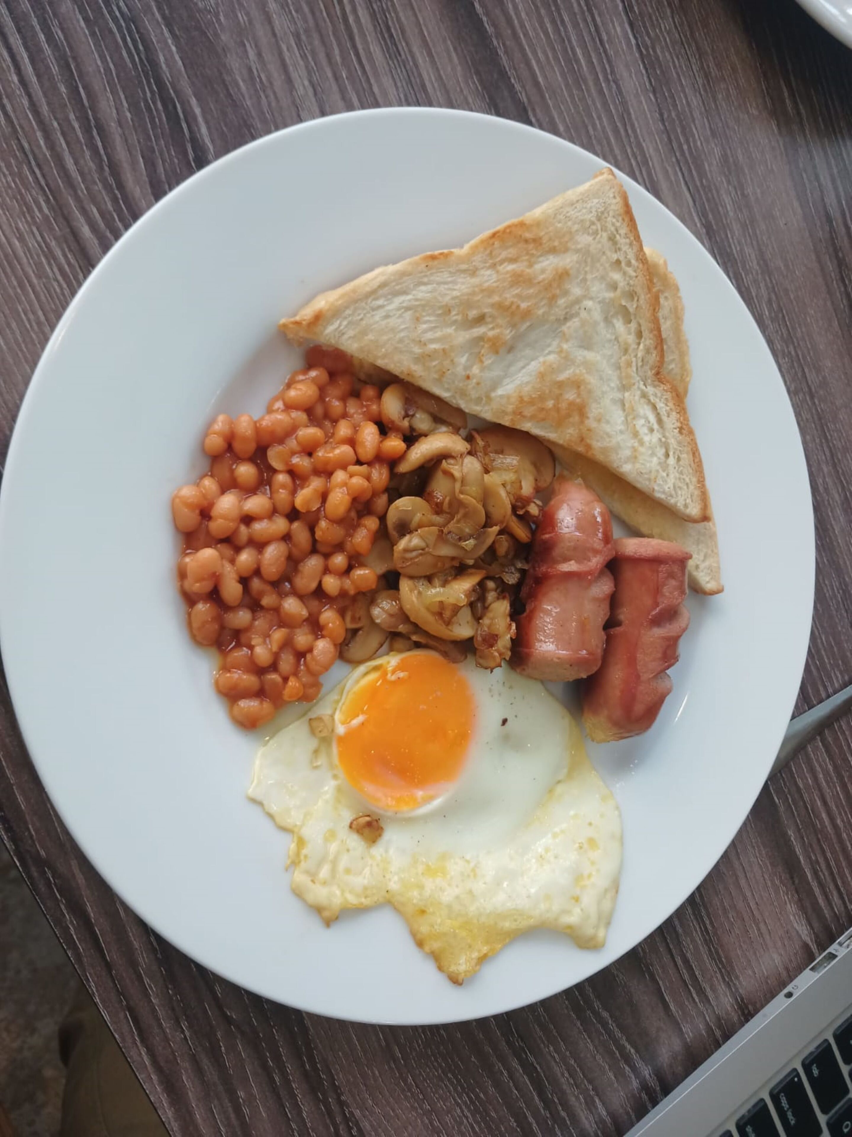 A plate with toast, beans, bacon, and a fried egg.