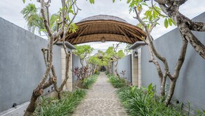 Un sendero bordeado de árboles y una estructura cubierta, que conduce a un edificio de fachada gris.