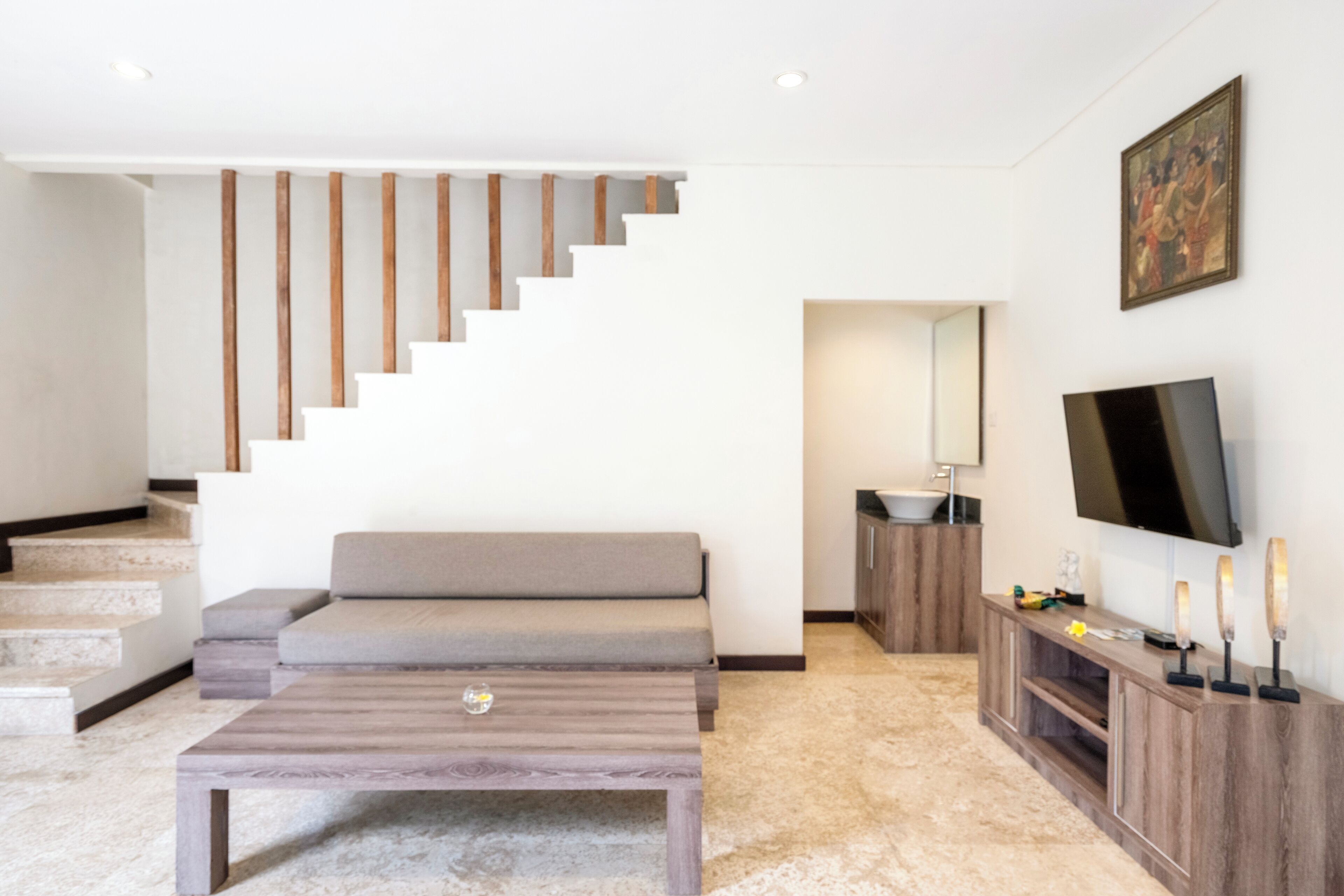 Una sala de estar moderna con una escalera, un sofá, una mesa de centro, un televisor y un armario.