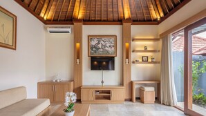 Una sala de estar moderna con techo de madera, televisor de pantalla plana, sofá, una mesa de centro con una orquídea en maceta y una puerta corrediza de vidrio que da a un espacio exterior.