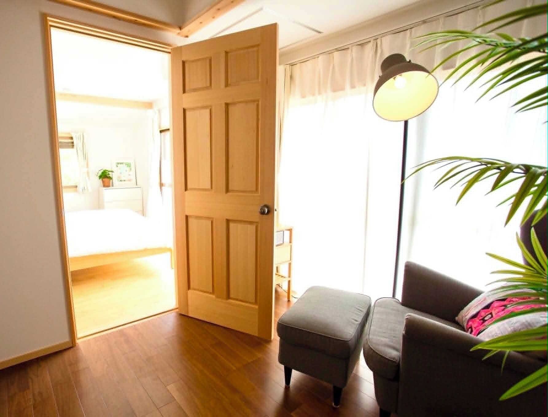 A room with a wooden floor, a closed door, a grey sofa, a small ottoman, and a lamp.