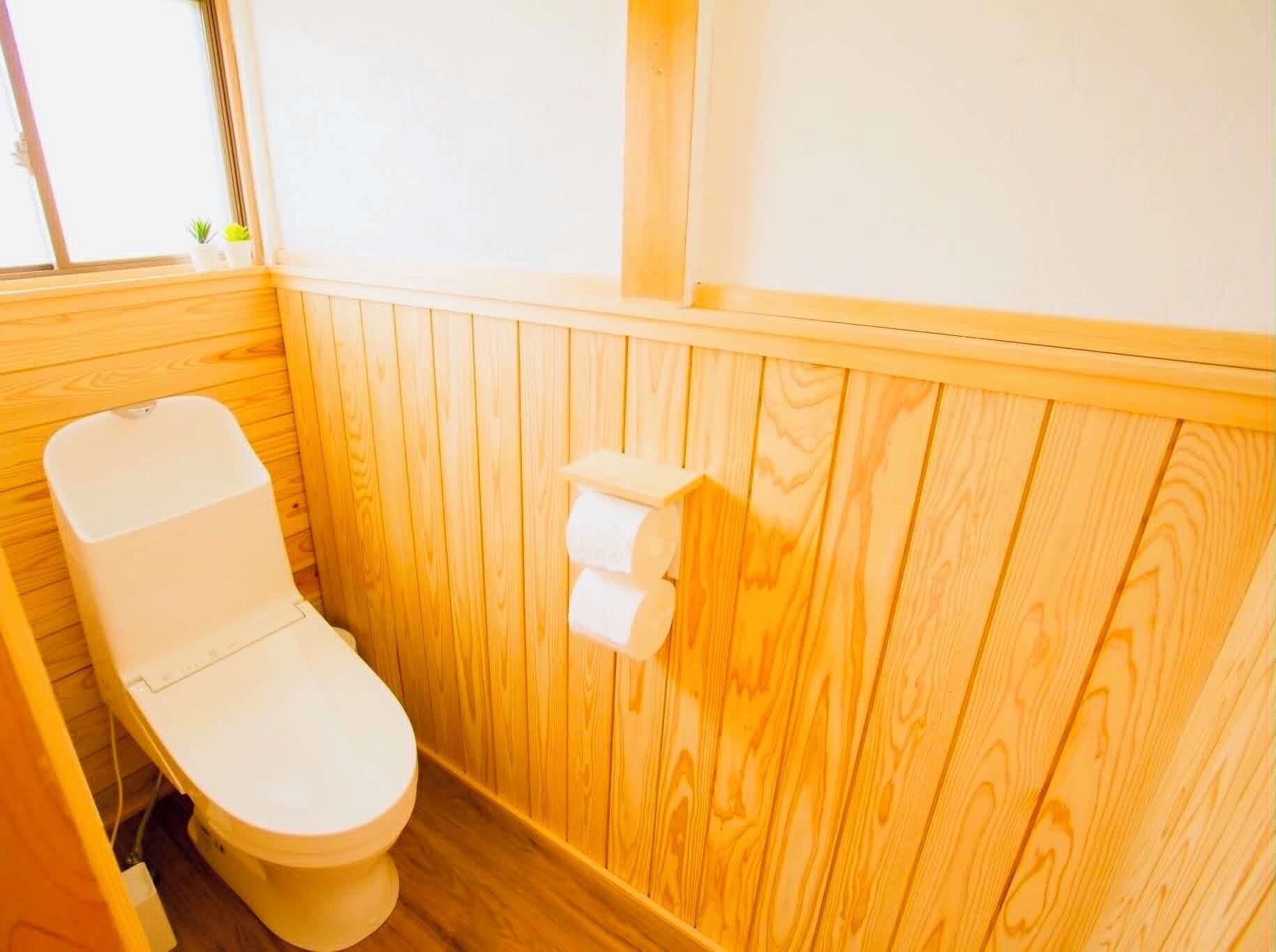 A wooden-paneled bathroom with a toilet, a small shelf with a plant, and a window.