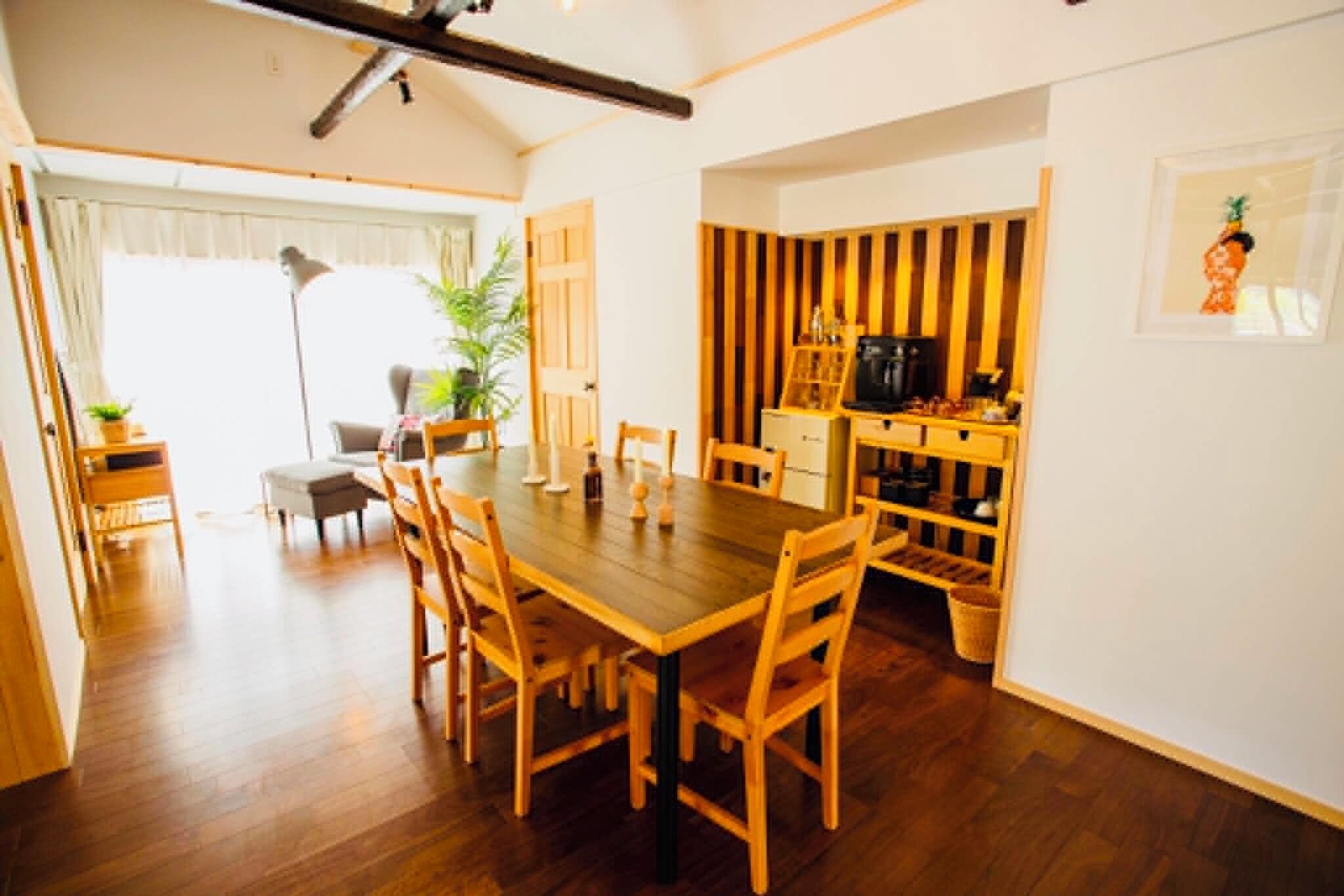Un comedor con mesa y sillas de madera, una cocina con cafetera y un ventanal con cortinas.