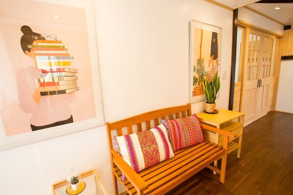A wooden bench with colorful cushions, a small table with a potted plant, and framed artwork on the wall. - Fully-rentable accommodation Kanata Riverview House (Kawanehon)