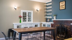 A dining area with a wooden table and chairs, a white cabinet with glass doors, and a brick fireplace.