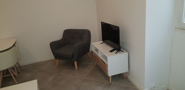 A small room with a dark armchair, a white TV stand, and a television.