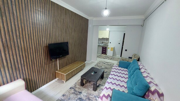 Un salon avec un téléviseur fixé au mur, un canapé agrémenté de coussins à motifs, une table basse et un tapis à motifs.