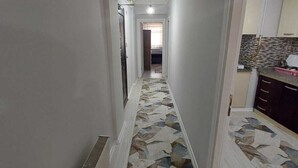 Un couloir étroit, dont le sol est décoré de motifs, mène à une cuisine.