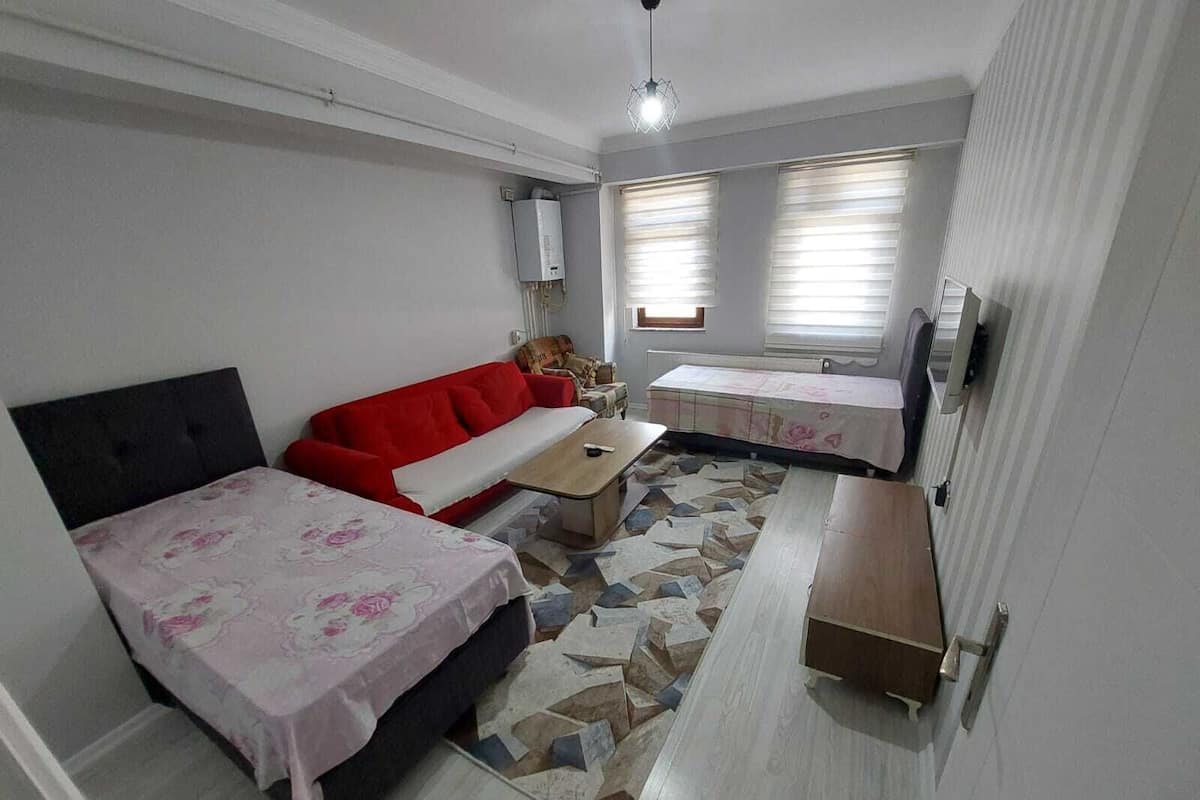 Una habitación compacta con cama, un sofá rojo, una mesita y un televisor.